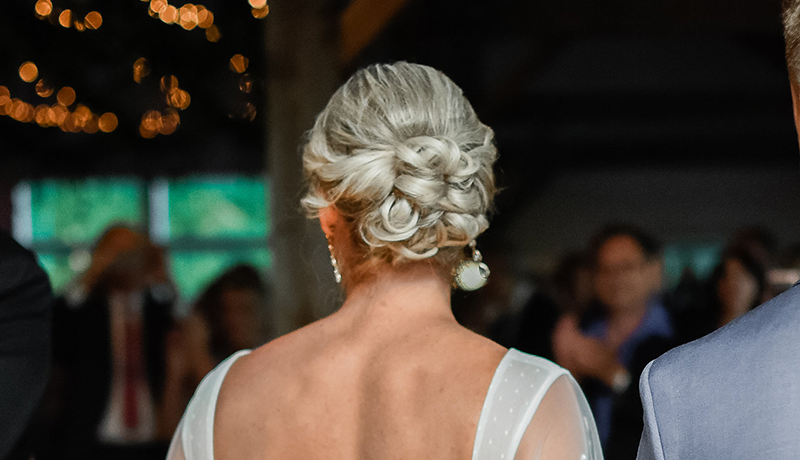 blonde woman with hair in braided updo wearing white backless dress.