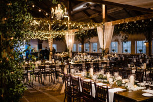 photo of wedding barn with lights, chandelier, and farmhouse tables with linens and candles