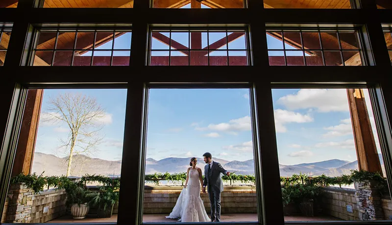 Photograph of Mountain Top Resort Jewel Guest Home. Features bride and groom on deck overlooking the Green mountains. Deck railing is covered in greenery.