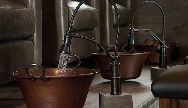 cooper pedicure bowl/basin with antique style gooseneck faucet running water. green leather armchairs and more basins in the background.